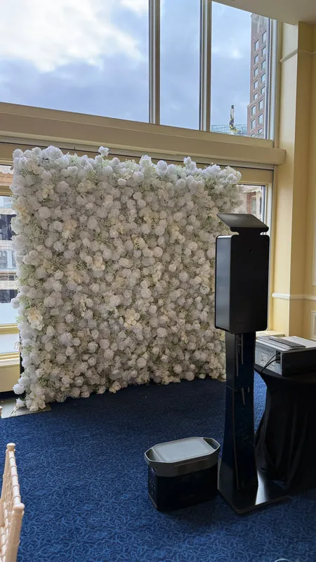 Flower wall booth installation with kiosk and white floral wall in an event space