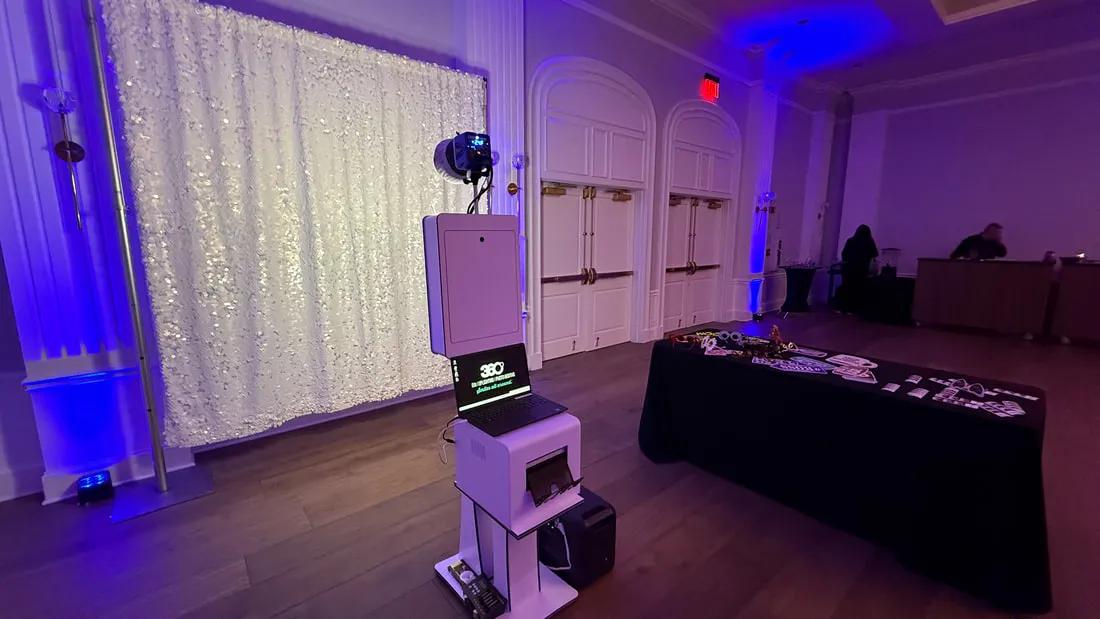 Open backdrop booth with white sequin wall, printer, and prop table in a ballroom