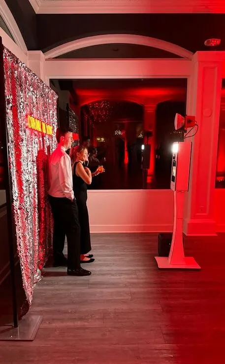 Open backdrop photo booth with silver sequin wall and dramatic red event lighting